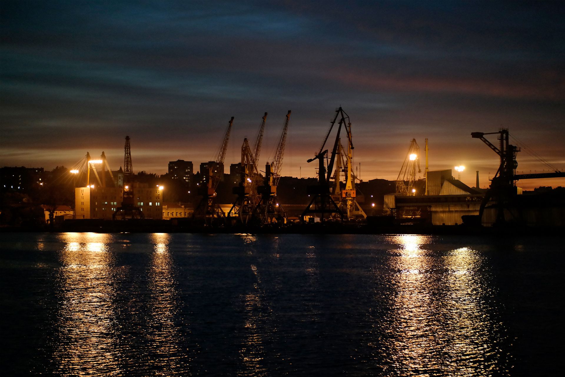 Port cranes lit up at night across the water